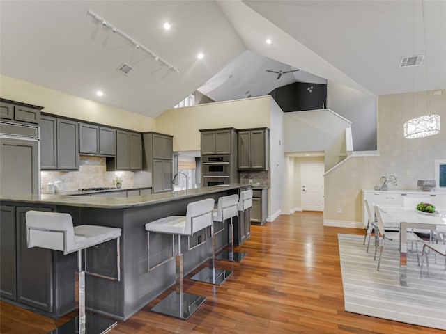 kitchen with wood finished floors, track lighting, a kitchen bar, appliances with stainless steel finishes, and visible vents