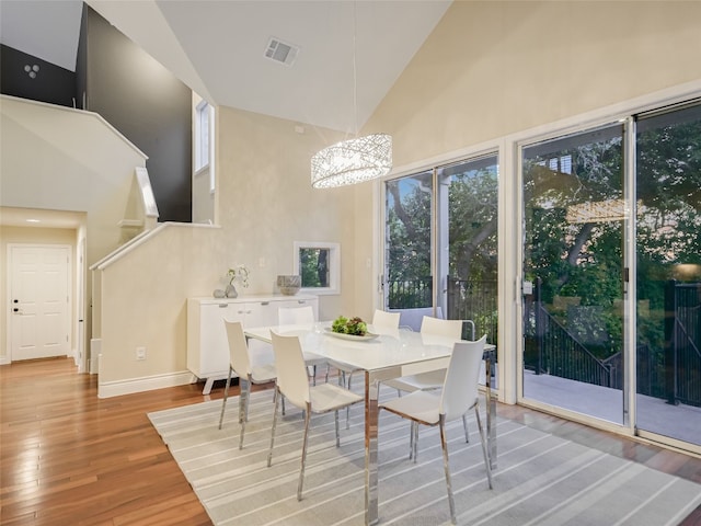 dining space with high vaulted ceiling, light wood-style floors, baseboards, a notable chandelier, and visible vents