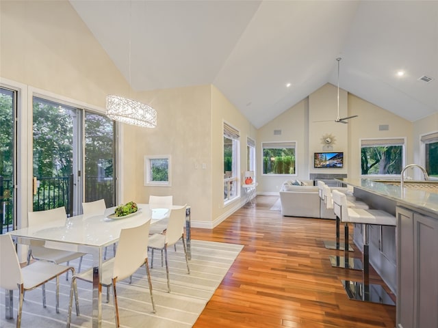 dining room with baseboards, light wood-type flooring, visible vents, and high vaulted ceiling