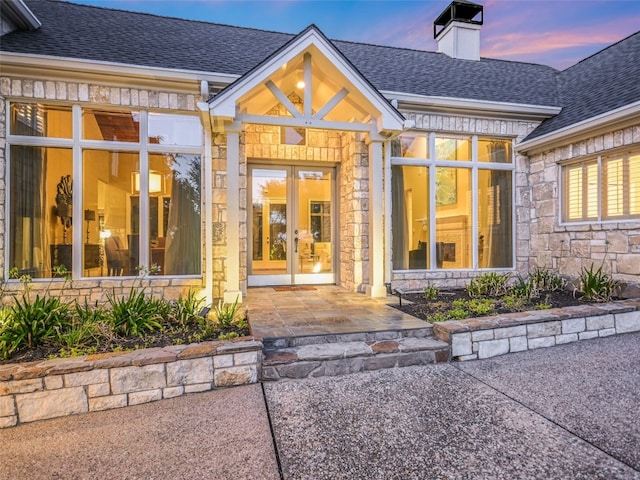 417 Beardsley Ln, Austin, TX 78746 - property entrance featuring french doors, stone siding, a chimney, and roof with shingles