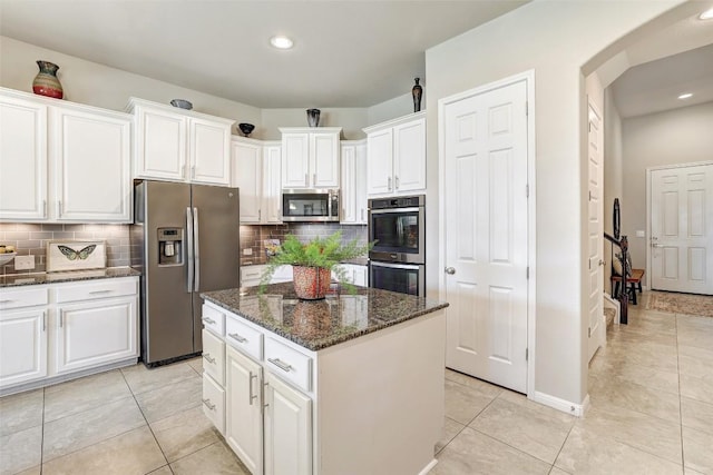 kitchen with light tile patterned floors, white cabinetry, dark stone countertops, stainless steel appliances, and a kitchen island