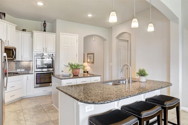 kitchen featuring pendant lighting, sink, white cabinetry, stainless steel appliances, and an island with sink