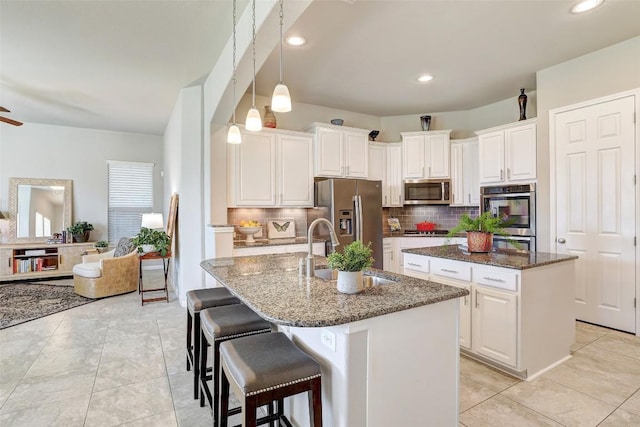 kitchen featuring white cabinetry, appliances with stainless steel finishes, a kitchen island with sink, and dark stone counters