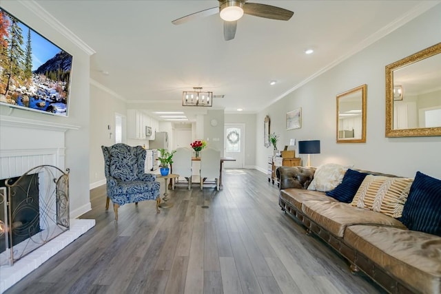 living room featuring crown molding, wood-type flooring, ceiling fan with notable chandelier, and a brick fireplace