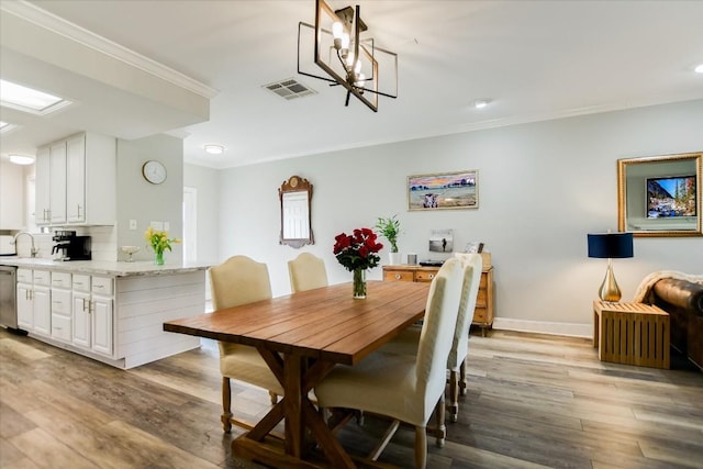 dining space with sink, light hardwood / wood-style flooring, ornamental molding, and a chandelier