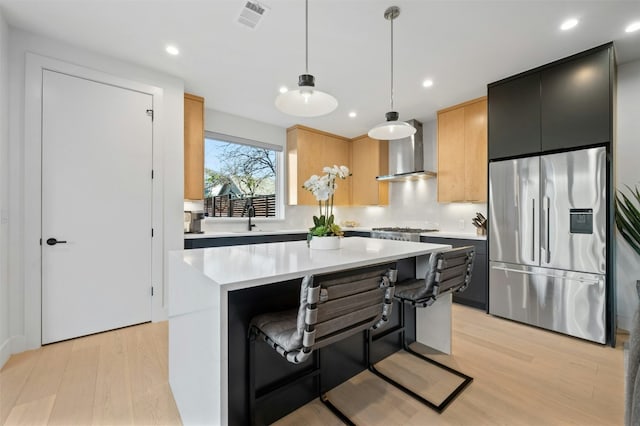 kitchen featuring a breakfast bar, stainless steel appliances, a kitchen island, decorative light fixtures, and wall chimney exhaust hood