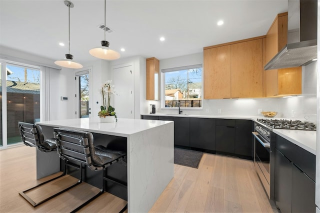 kitchen featuring high end stainless steel range, a breakfast bar area, hanging light fixtures, a kitchen island, and wall chimney range hood