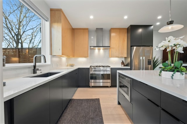 kitchen featuring light brown cabinetry, sink, decorative light fixtures, high quality appliances, and wall chimney range hood