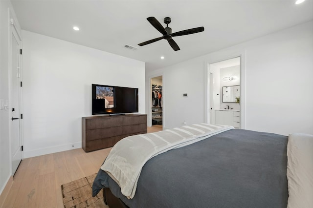 bedroom with ceiling fan, ensuite bathroom, a walk in closet, a closet, and light wood-type flooring