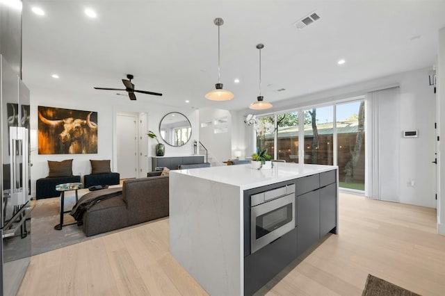 kitchen with a center island, light hardwood / wood-style flooring, stainless steel microwave, gray cabinets, and pendant lighting