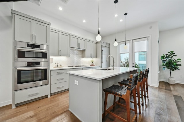 kitchen with gray cabinets, pendant lighting, sink, a kitchen island with sink, and stainless steel appliances