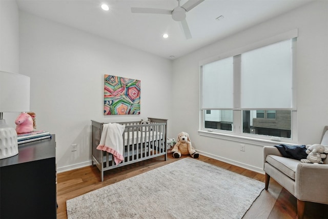 bedroom with a nursery area, ceiling fan, and hardwood / wood-style floors