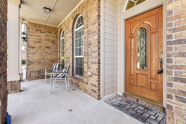 doorway to property featuring a porch and brick siding