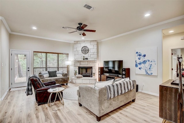 living room with crown molding, a stone fireplace, ceiling fan, and light wood-type flooring