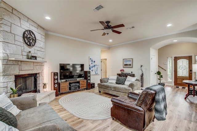 living room featuring ceiling fan, ornamental molding, a stone fireplace, and light wood-type flooring