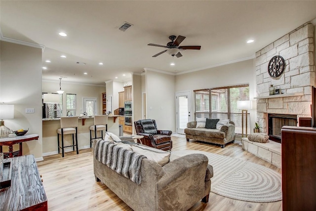 living room with crown molding, a stone fireplace, ceiling fan, and light hardwood / wood-style floors