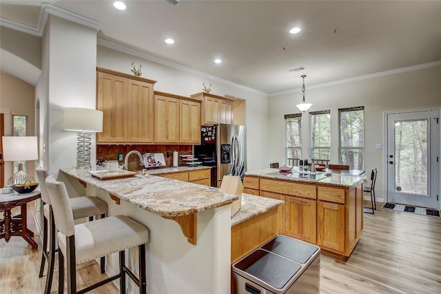 kitchen with pendant lighting, stainless steel fridge, light stone counters, ornamental molding, and kitchen peninsula