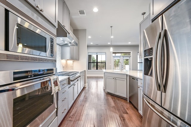 kitchen with decorative light fixtures, backsplash, stainless steel appliances, light stone countertops, and dark wood-type flooring