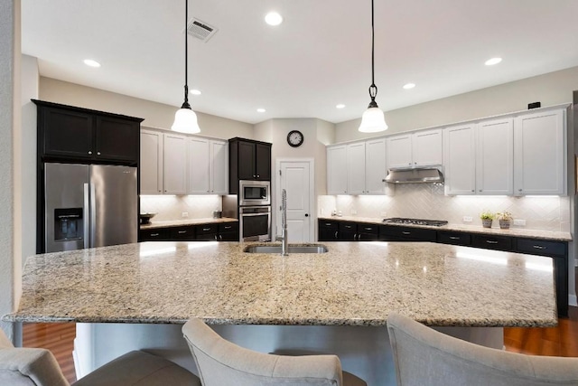 kitchen featuring stainless steel appliances, a kitchen breakfast bar, a large island with sink, and decorative light fixtures