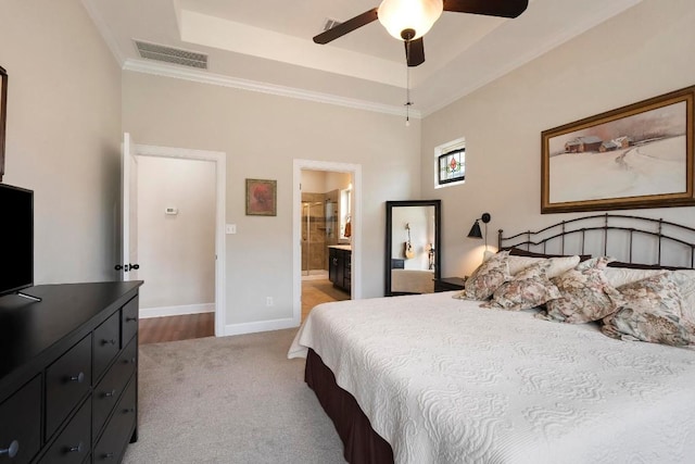 bedroom with crown molding, ensuite bath, a tray ceiling, carpet floors, and ceiling fan