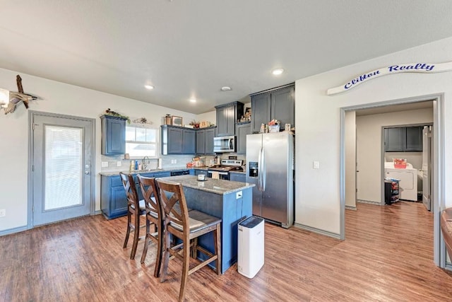 kitchen featuring sink, a center island, a kitchen breakfast bar, stainless steel appliances, and washer and clothes dryer