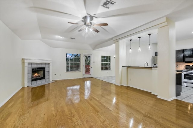 unfurnished living room with a tile fireplace, ceiling fan, and light hardwood / wood-style flooring