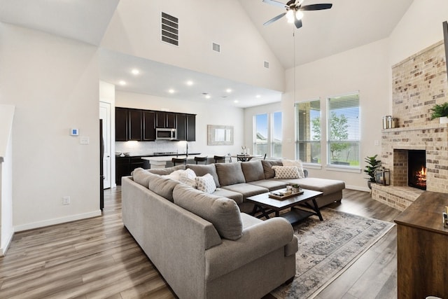 living room with hardwood / wood-style flooring, a fireplace, high vaulted ceiling, and ceiling fan