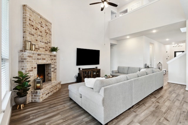 living room featuring hardwood / wood-style floors, a high ceiling, a brick fireplace, and ceiling fan