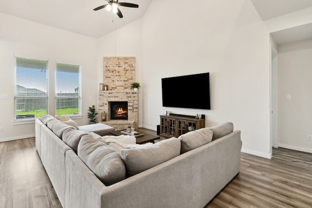 living room featuring hardwood / wood-style flooring, ceiling fan, high vaulted ceiling, and a brick fireplace