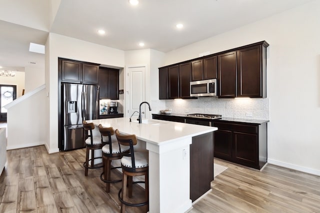 kitchen featuring appliances with stainless steel finishes, tasteful backsplash, an island with sink, sink, and dark brown cabinets