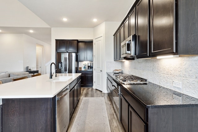 kitchen with sink, light hardwood / wood-style flooring, stainless steel appliances, tasteful backsplash, and an island with sink