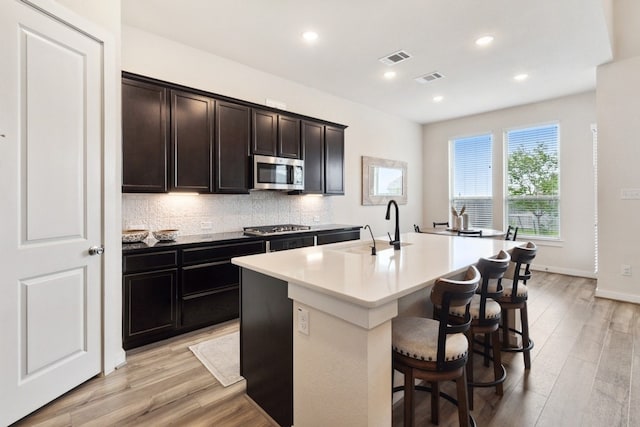 kitchen featuring sink, appliances with stainless steel finishes, a kitchen breakfast bar, an island with sink, and decorative backsplash