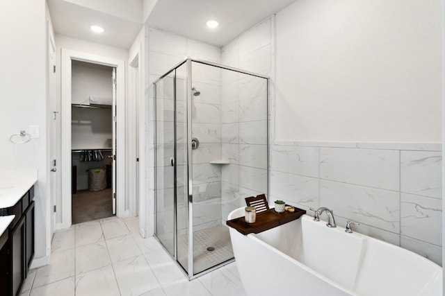 bathroom featuring plus walk in shower, tile walls, and vanity