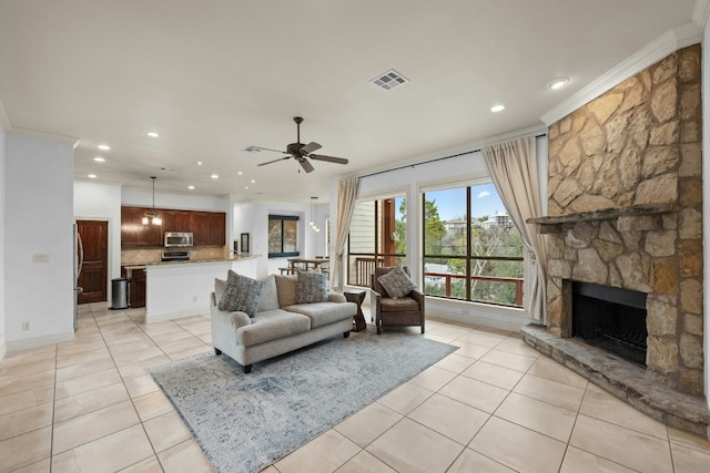 tiled living room featuring a stone fireplace, ornamental molding, and ceiling fan