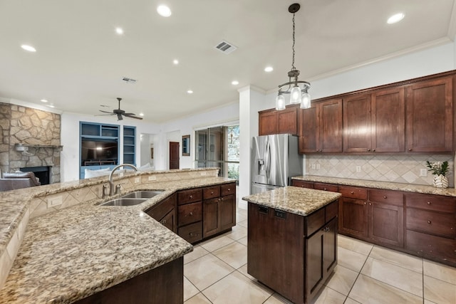 kitchen featuring sink, decorative light fixtures, a center island, stainless steel fridge, and light stone countertops