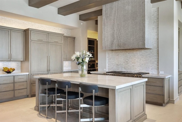 kitchen with a kitchen island, a breakfast bar, decorative backsplash, stainless steel gas cooktop, and beam ceiling