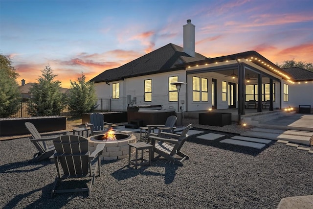 back house at dusk featuring an outdoor fire pit, a hot tub, and a patio area