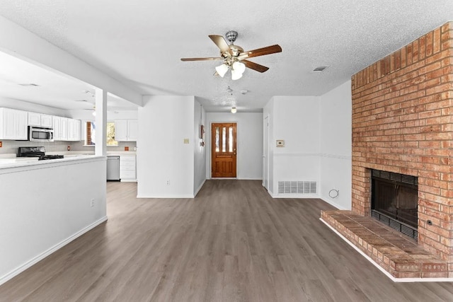 unfurnished living room with dark wood-type flooring, a healthy amount of sunlight, a brick fireplace, and a textured ceiling