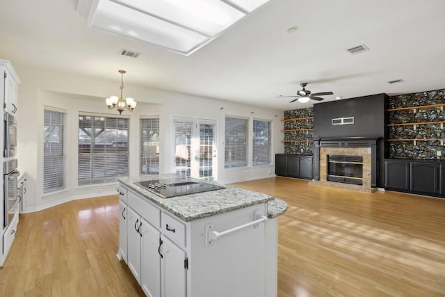 kitchen featuring decorative light fixtures, white cabinets, a center island, a brick fireplace, and black electric cooktop