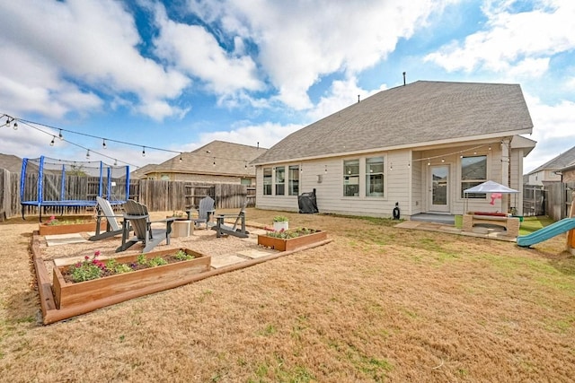 rear view of house with an outdoor fire pit, a patio area, a trampoline, and a lawn