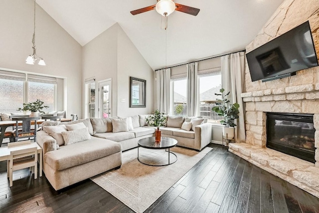 living room with ceiling fan with notable chandelier, a stone fireplace, high vaulted ceiling, and dark hardwood / wood-style flooring