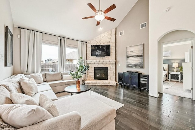 living room featuring a stone fireplace, dark wood-type flooring, high vaulted ceiling, and ceiling fan