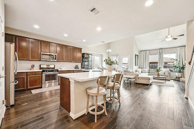 kitchen featuring an island with sink, appliances with stainless steel finishes, a breakfast bar, and dark wood-type flooring