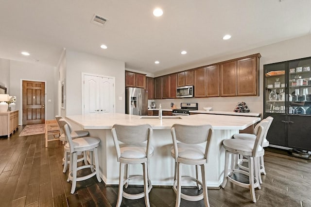 kitchen with a spacious island, a kitchen bar, sink, appliances with stainless steel finishes, and dark hardwood / wood-style flooring