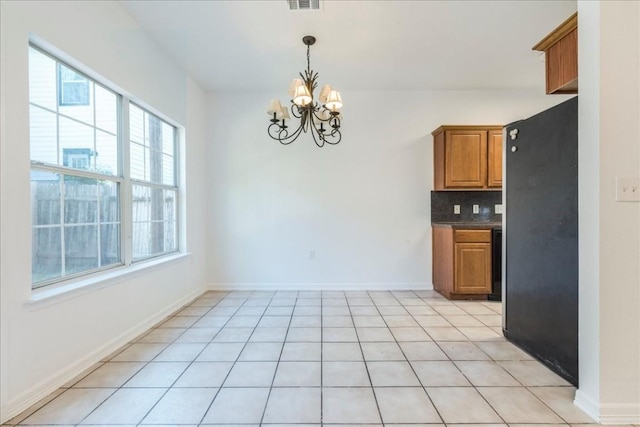 kitchen featuring an inviting chandelier, decorative light fixtures, light tile patterned floors, black refrigerator, and backsplash