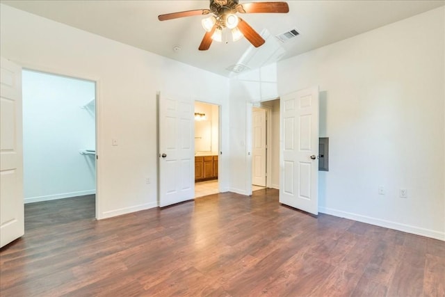 unfurnished bedroom featuring ensuite bath, dark wood-type flooring, ceiling fan, and a spacious closet