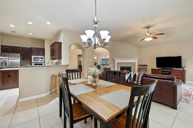 tiled dining space featuring a tiled fireplace, sink, ceiling fan with notable chandelier, and lofted ceiling