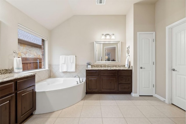 bathroom with tile patterned flooring, vanity, lofted ceiling, and a bathtub