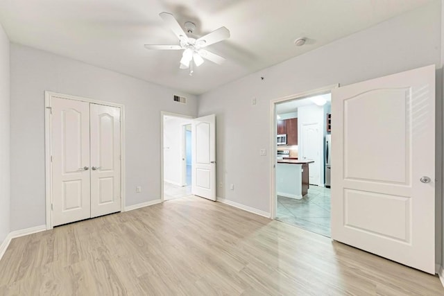 unfurnished bedroom with ceiling fan, a closet, light hardwood / wood-style flooring, and stainless steel refrigerator