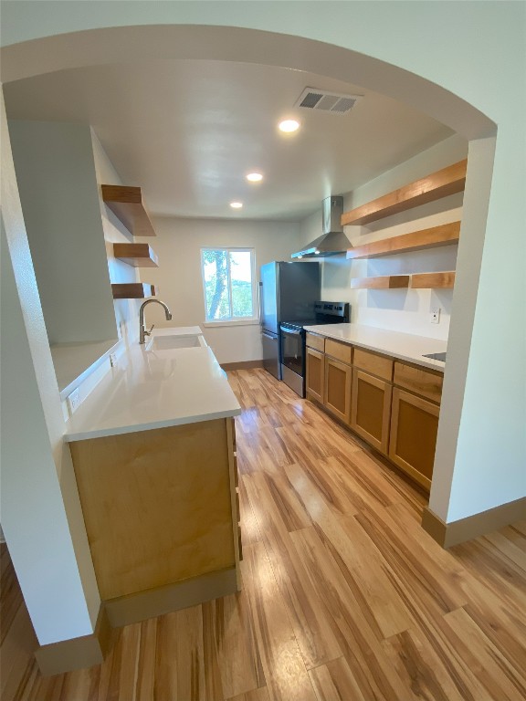 5801 Thunderbird St Unit A15, Lago Vista, TX 78645 - kitchen featuring open shelves, appliances with stainless steel finishes, wall chimney exhaust hood, light wood-style floors, and arched walkways